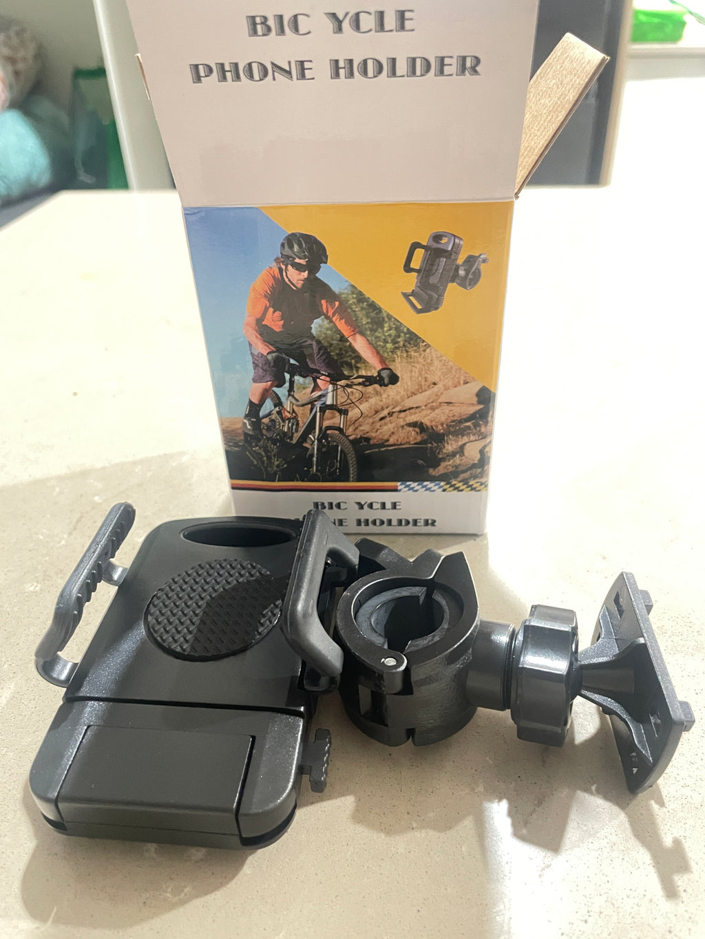 Black bicycle phone holder on a shelf with a book titled 'Bicycle Phone Holder' in the background.